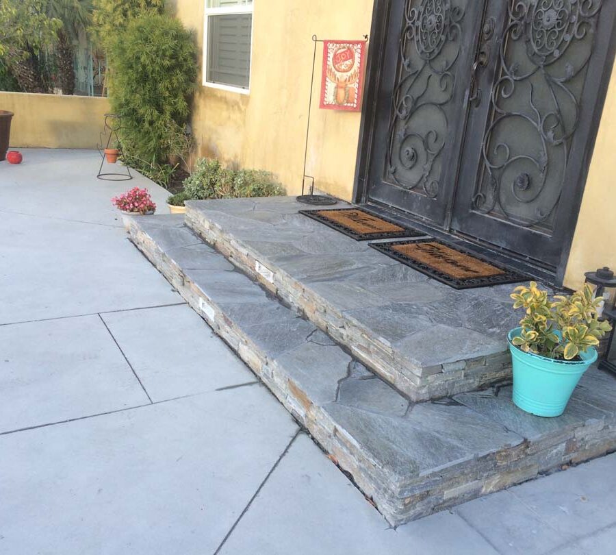 New concrete backyard patio with beautiful flagstone covered concrete steps with stone veneer and a new artisan door. Pacificland Constructors