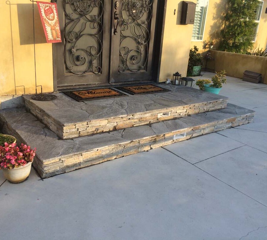 New concrete backyard patio with beautiful flagstone covered concrete steps with stone veneer and a new artisan door. Pacificland Constructors