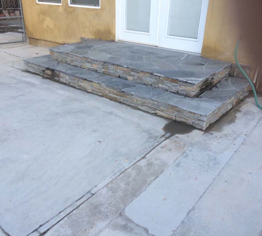 New stone veneer on the face of new concrete steps under an old door that will be replaced. Pacificland Constructors