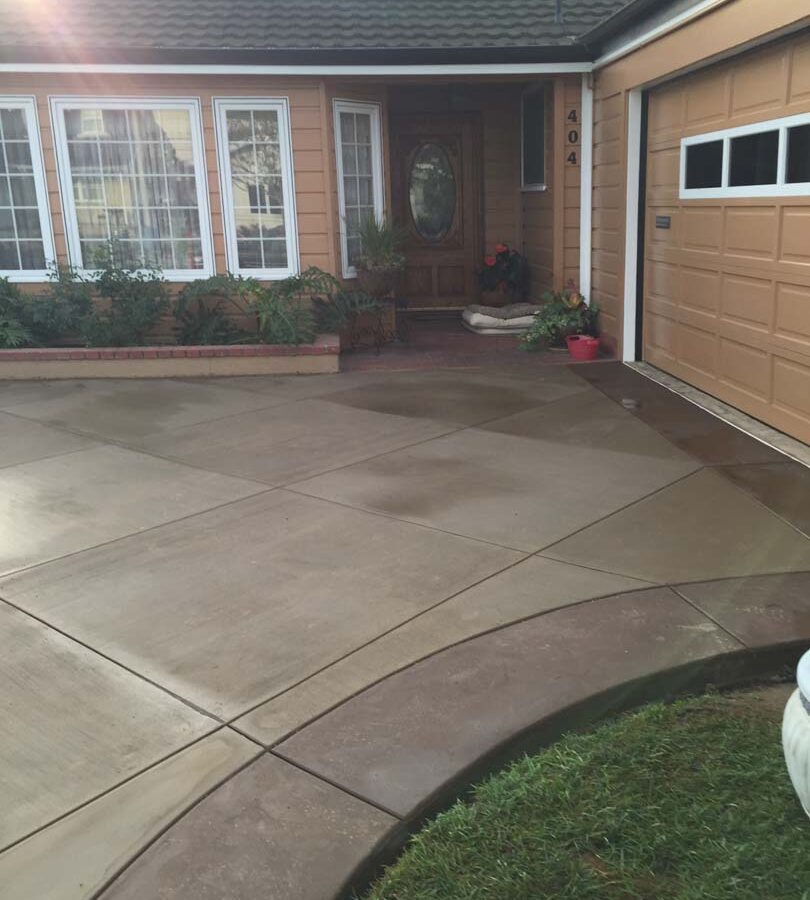 New colored concrete driveway with diamond pattern and a contrasting ribbon around the perimeter. The surface is broom swept and has hand scorched joints. Pacificland Constructors