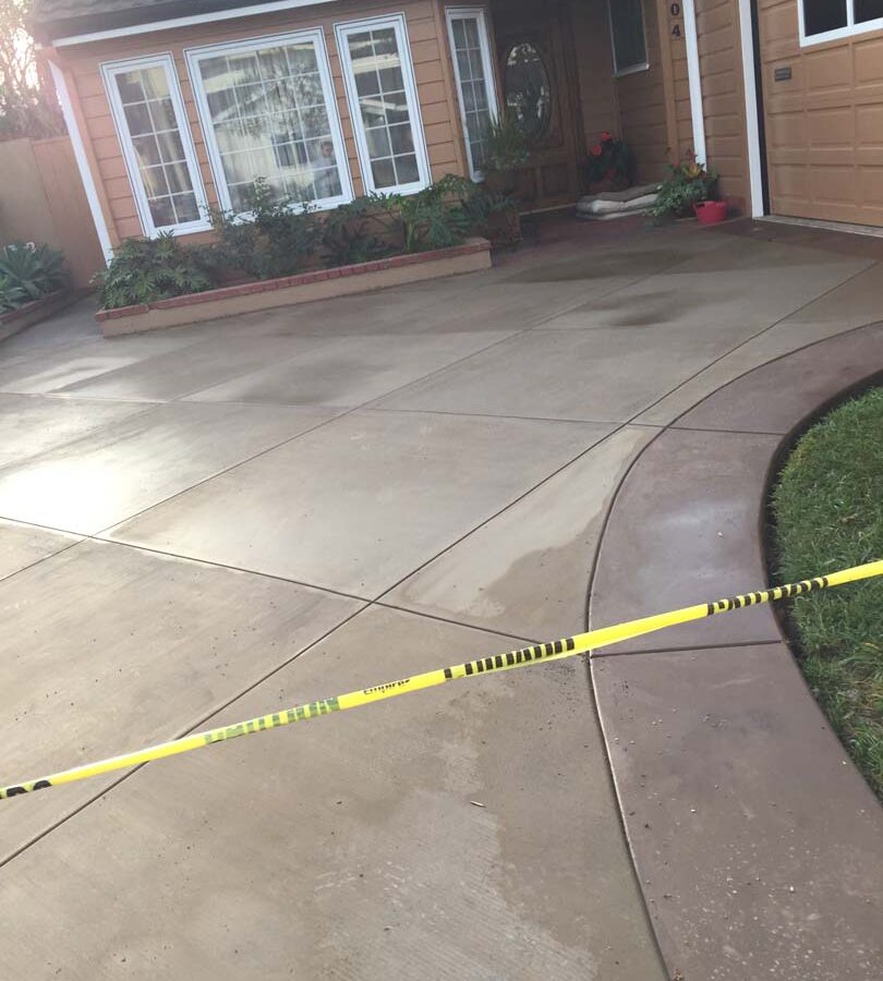 New colored concrete driveway with diamond pattern and a contrasting ribbon around the perimeter. The surface is broom swept and has hand scorched joints. Pacificland Constructors