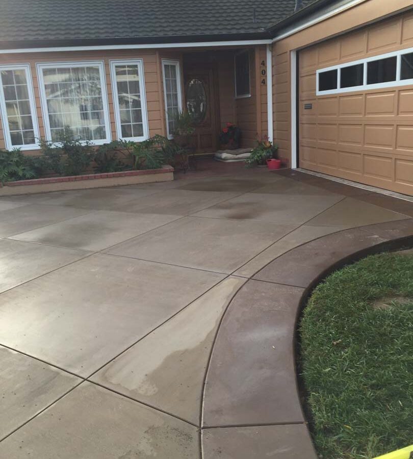 New colored concrete driveway with diamond pattern and a contrasting ribbon around the perimeter. The surface is broom swept and has hand scorched joints. Pacificland Constructors